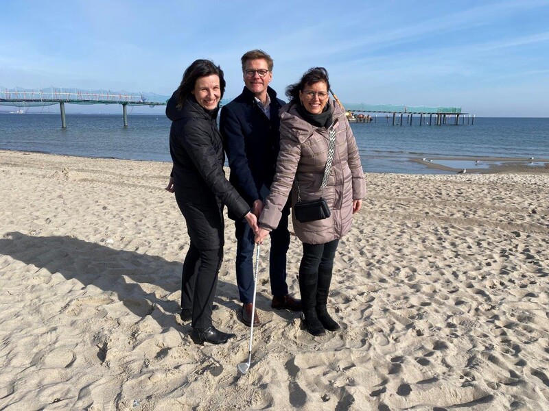 Zwei Frauen und ein Mann halten zusammen einen Golfschläger am Strand