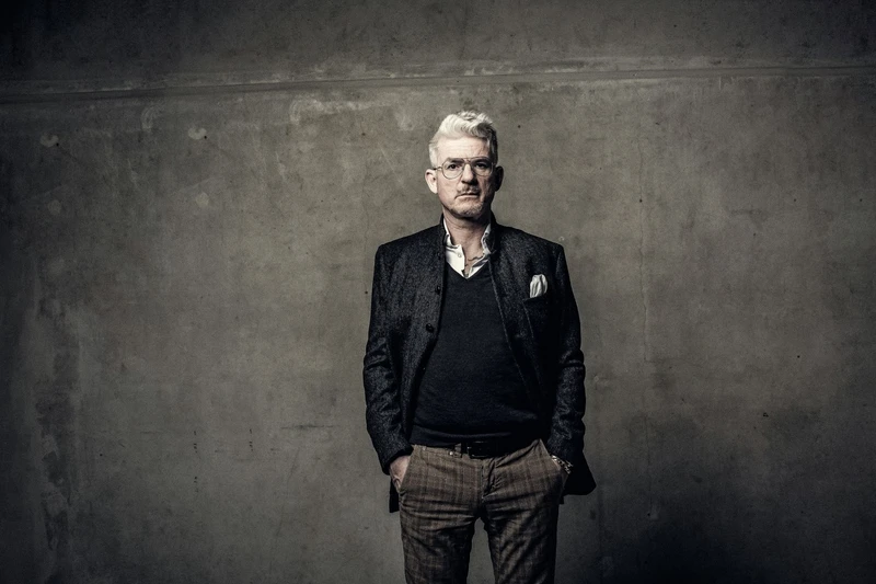 Porträtfoto von Heinz Strunk vor einer grauen Wand