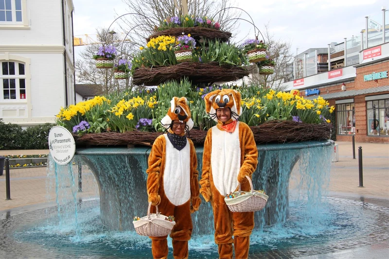 Zwei als Osternhasen verkleidete Menschen stehen vor dem Osterbrunnen