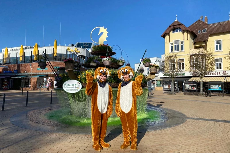 Zwei als Hasen verkleidete Personen stehen auf dem Timmendorfer Marktplatz vor dem Brunnen