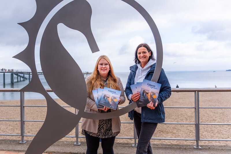 Projektmanagerin Lale Schoenberg und Marketing Leiterin Silke Szymoniak präsentieren das neue Strand Magazin.