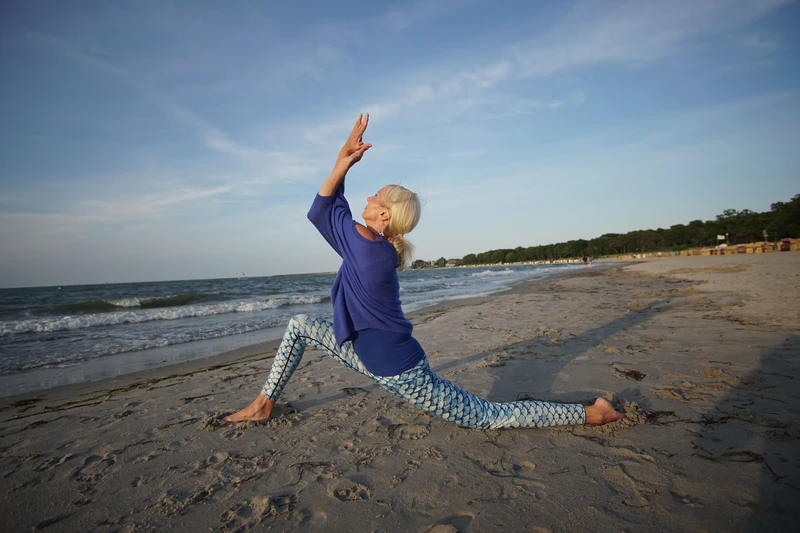 Frau macht Yoga an Kraftort Strand vor blauem Himmel