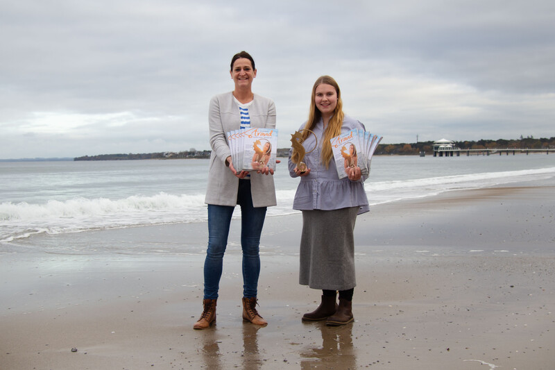 Silke Szymoniak und Lale Schoenberg mit dem Strandmagazin2024 in der Hand am Strand