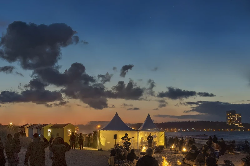 Der Strand am Abend mit einem Zelt und vielen kleinen Lichtquellen und Sitzgelegenheiten