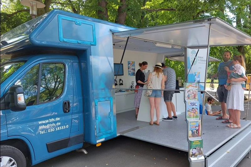 Blaues großes Wohnmobil als Infostand umgebaut mit einer kleinen Gruppe Menschen darin