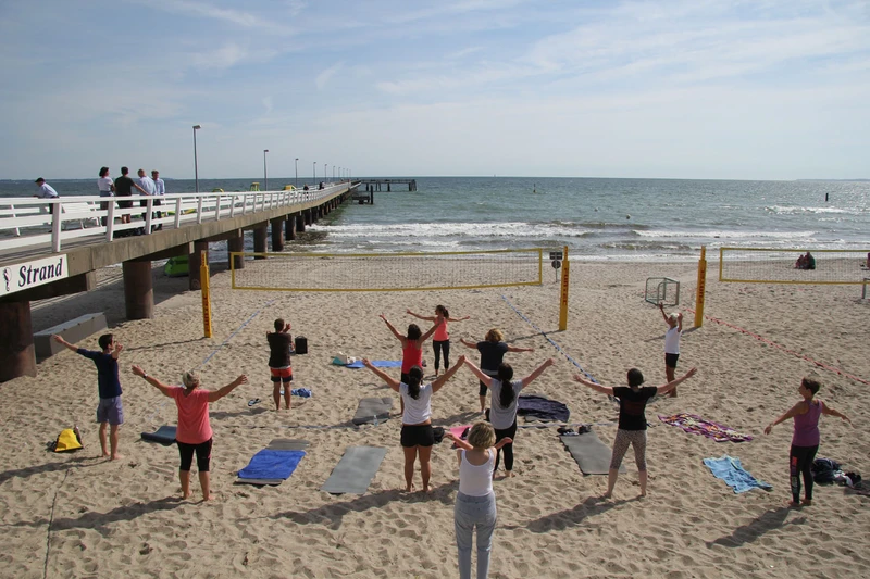 Eine Personengruppe macht Yoga am Strand neben der Seebrücke