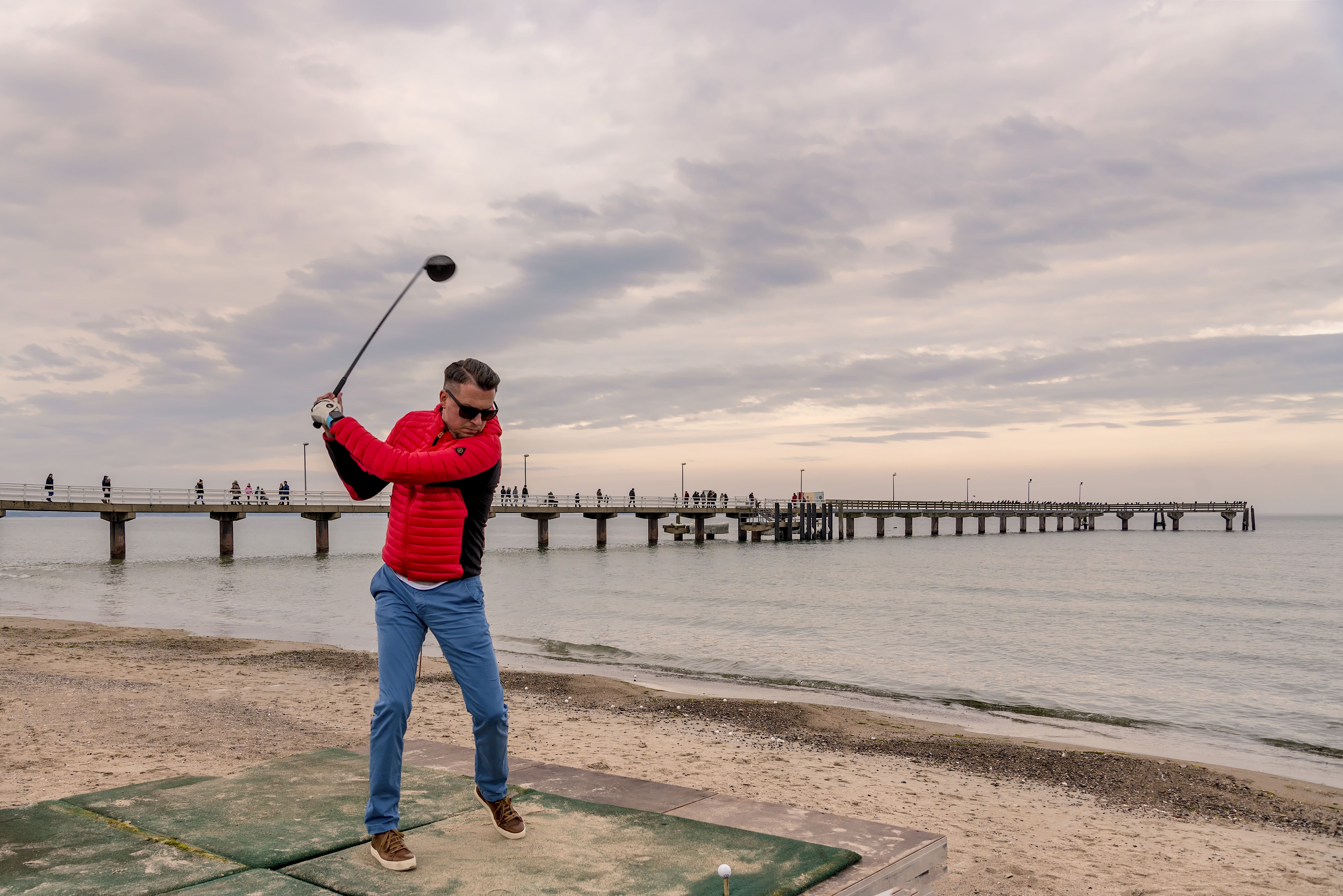 Ein Golfer holt aus um den Ball am Strand ins Wasser zu schlagen