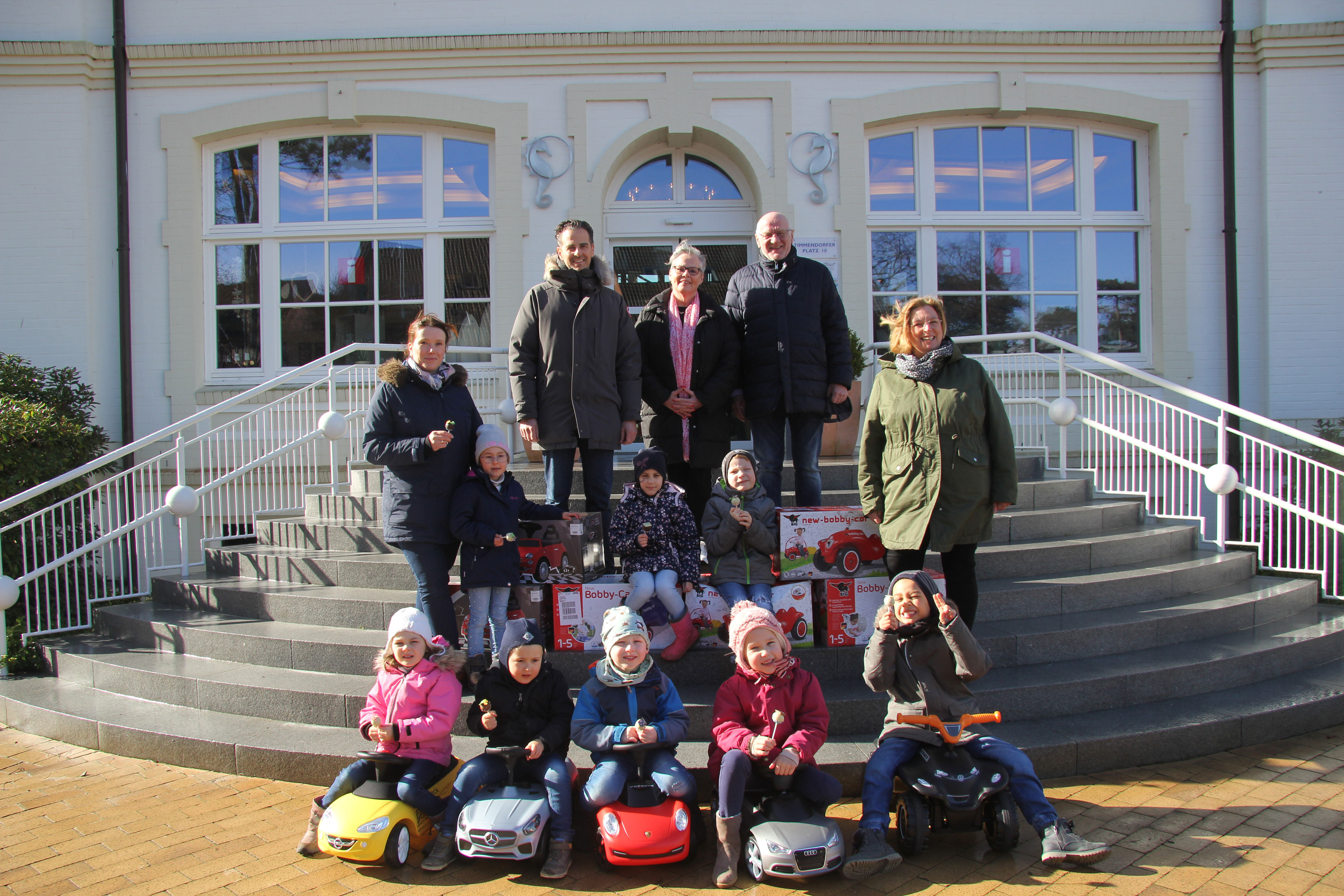 Gruppenfoto vor dem Rathaus mit Kindern auf Bobby Cars, die aussehen wie echte Autos