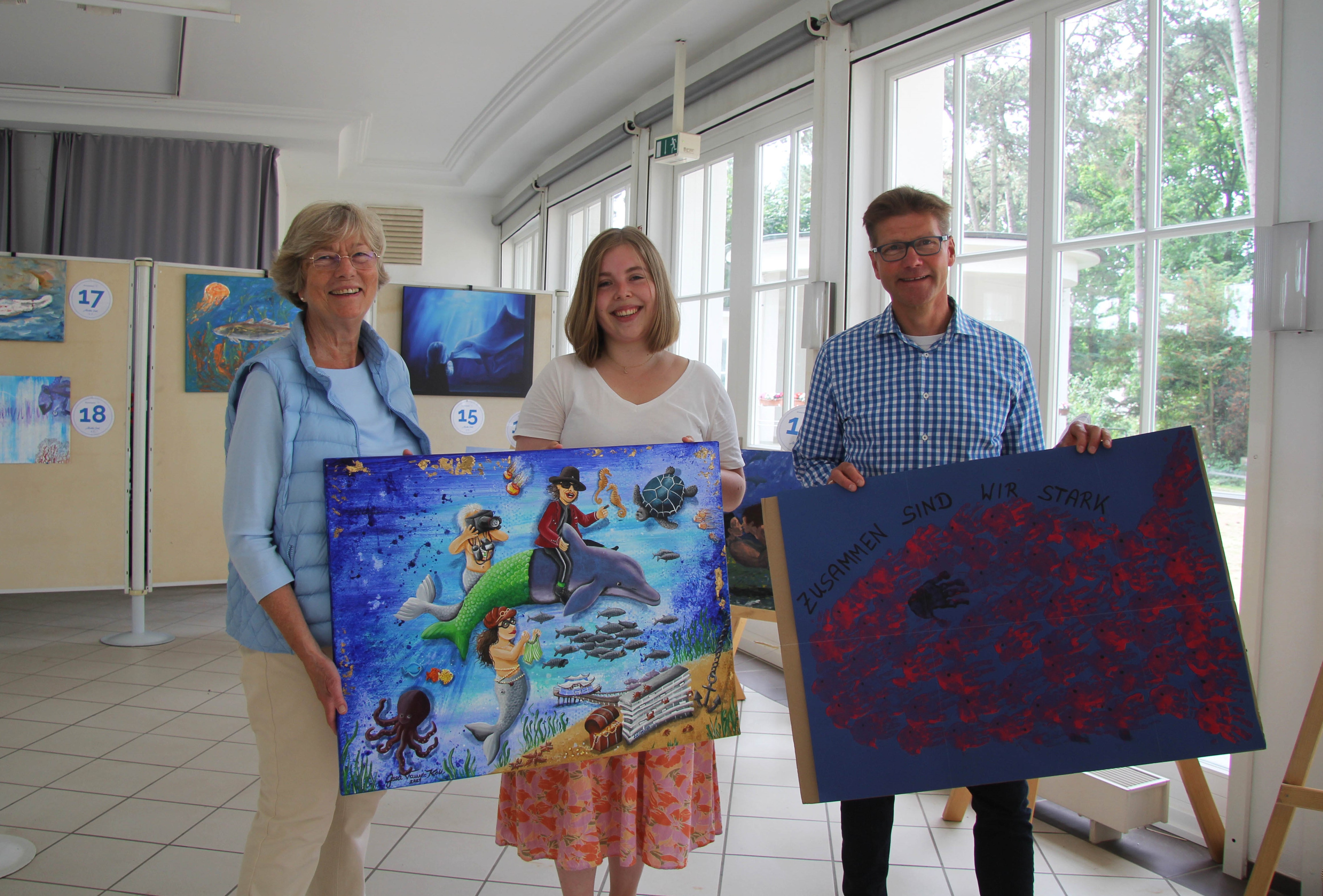 Drei Personen präsentieren zwei große Kunstwerke