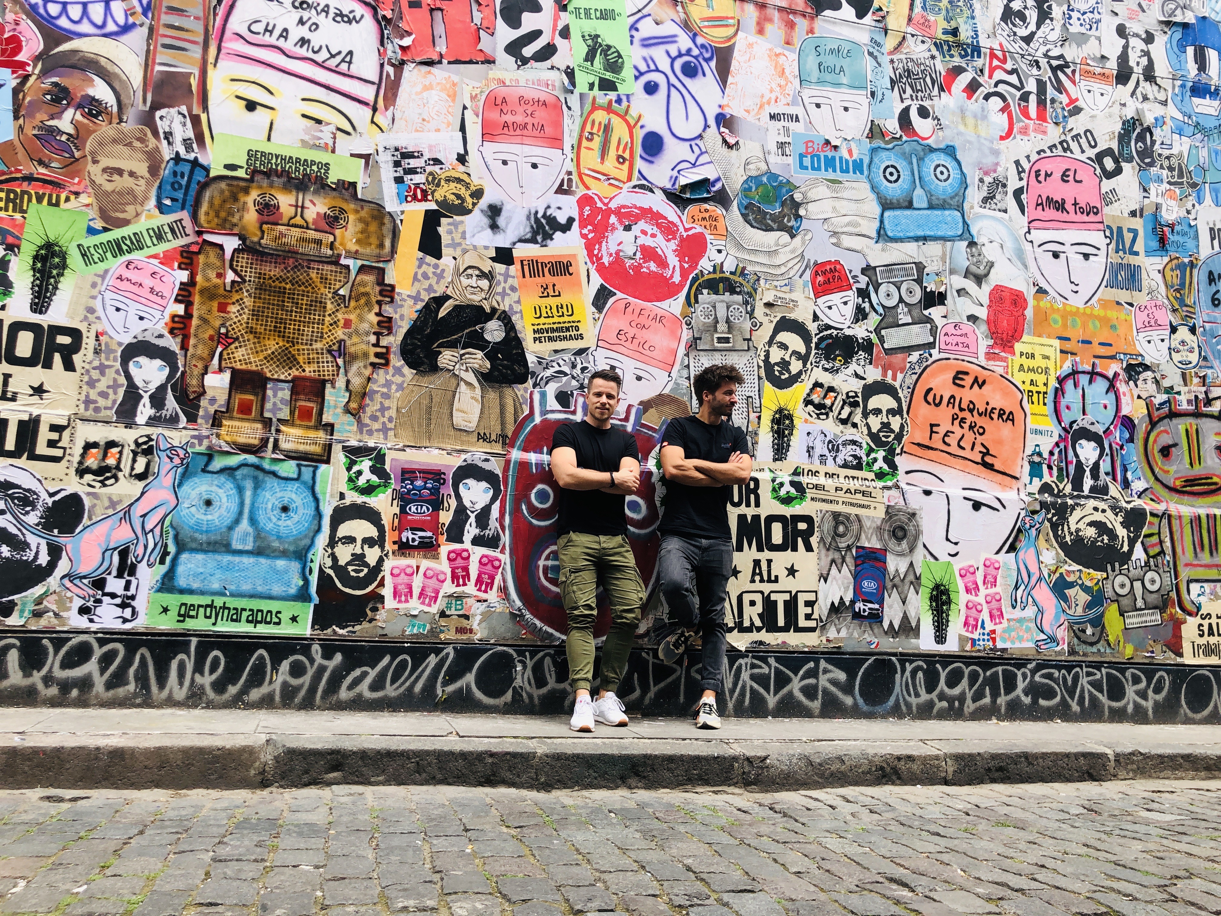 Zwei Männer angelehnt an eine Wand voller Plakate und Graffiti.