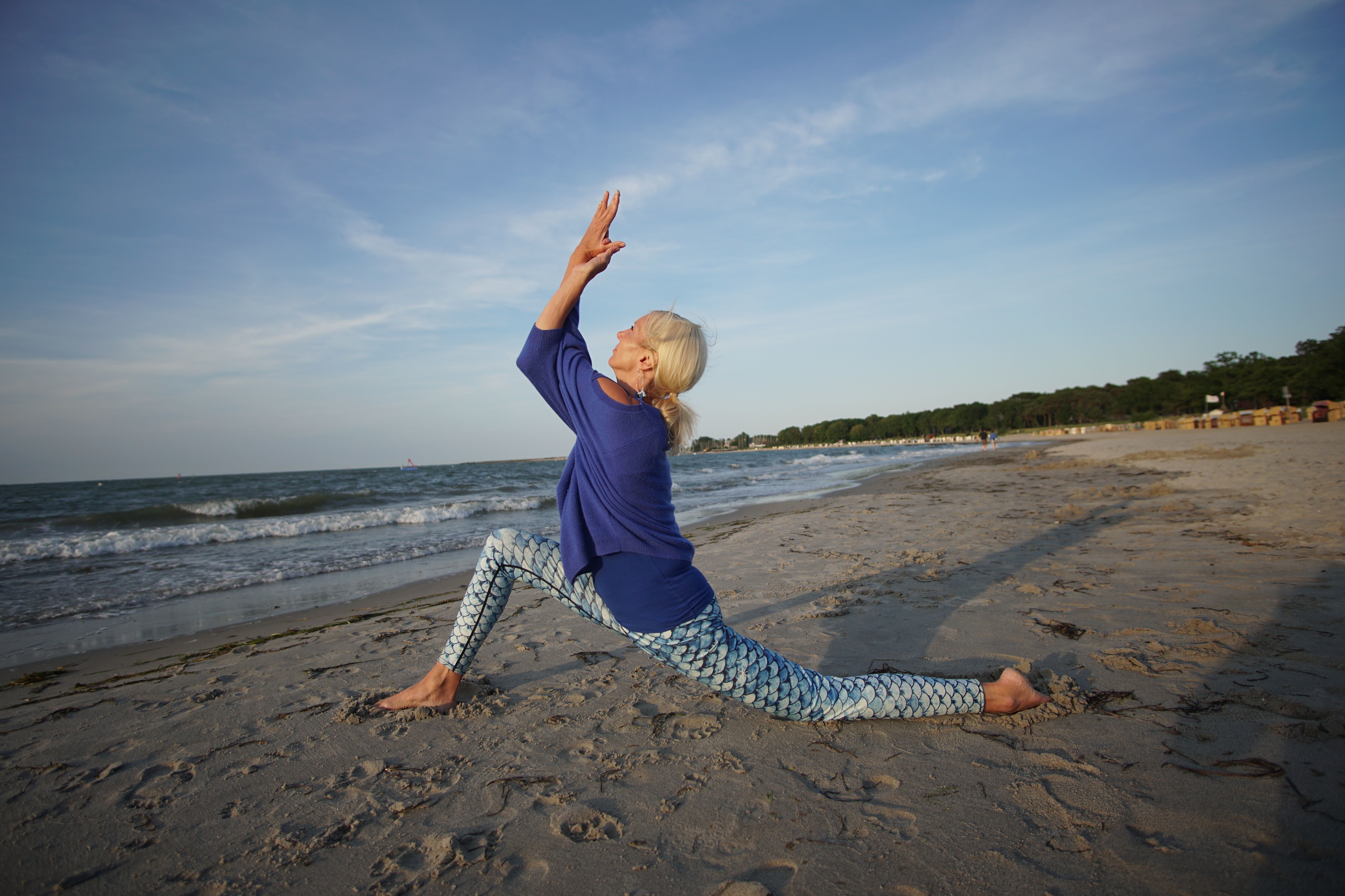 Frau macht Yoga an Kraftort Strand vor blauem Himmel