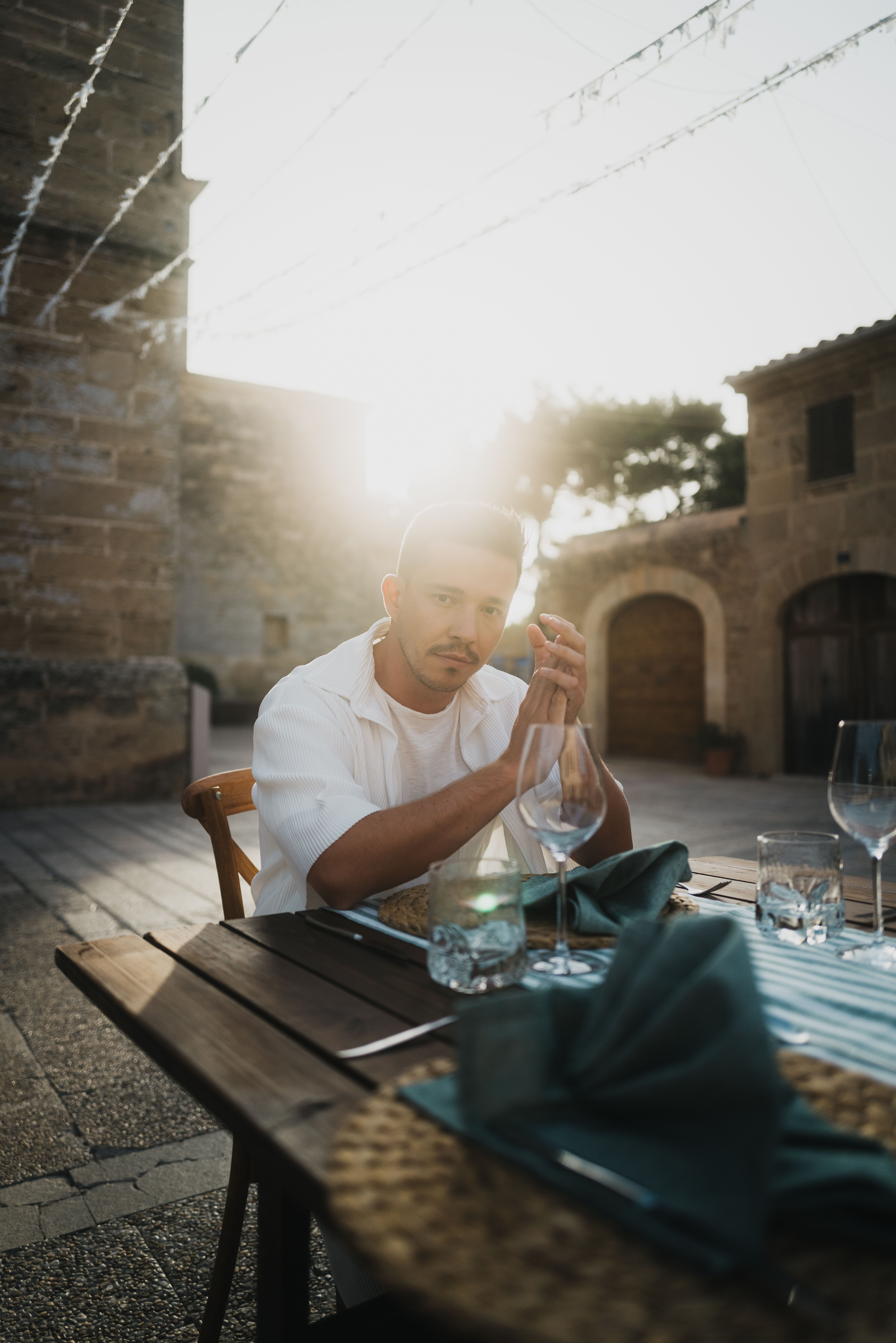 Mann sitzt in einem Innenhof an einem gedeckten Holztisch in der Abendsonne