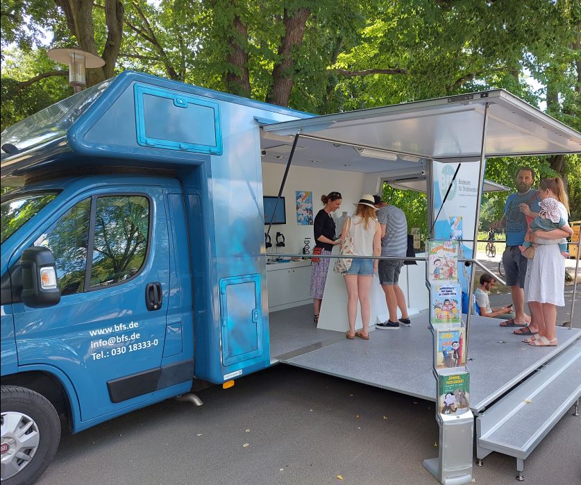 Blaues großes Wohnmobil als Infostand umgebaut mit einer kleinen Gruppe Menschen darin